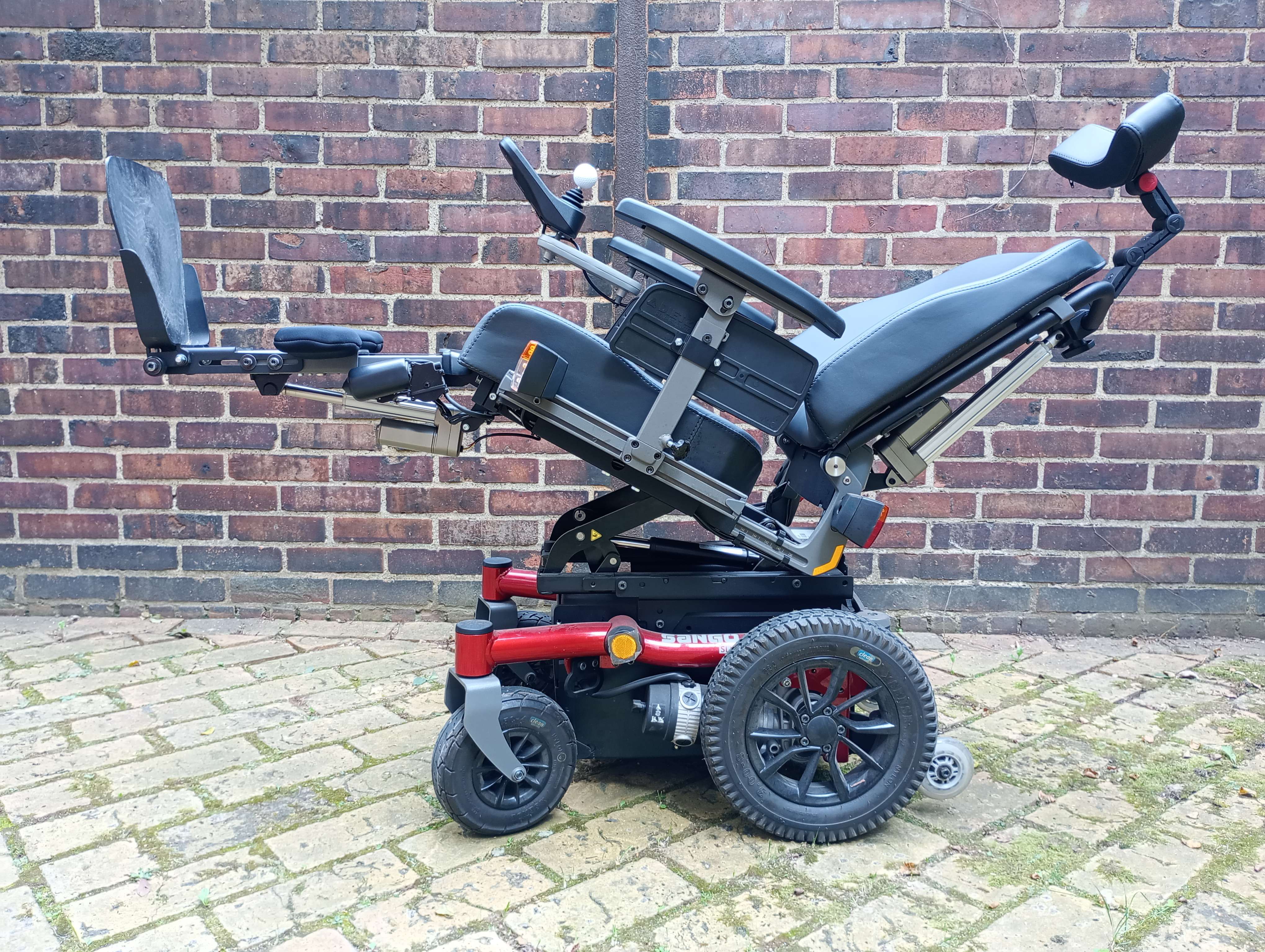 An empty electric reclining wheelchair beside a brick wall.